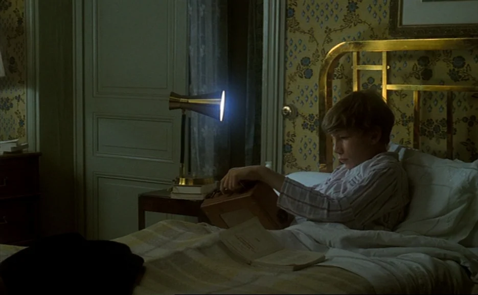 Murmur of the Heart (1971) movie still: medium — A child's bedroom features yellow wallpaper with a blue floral pattern and a brass bed frame. The…