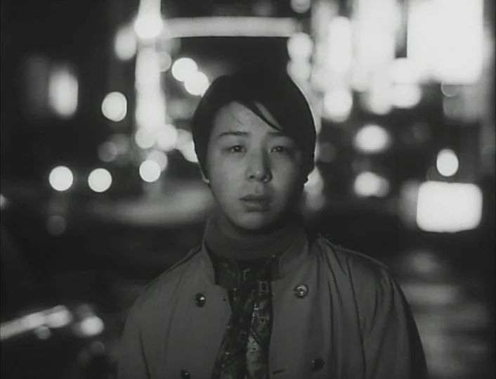 Funeral Parade of Roses (1969) movie still: closeup — An urban setting at night features blurred streetlights glowing softly in the dark background.…
