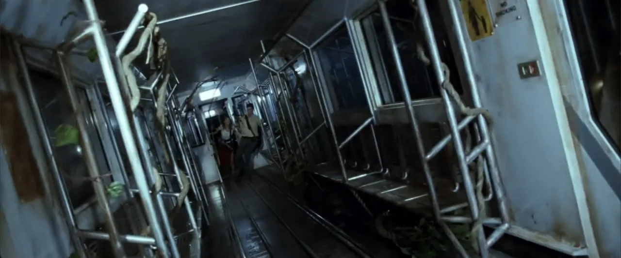 A Sound of Thunder (2005) movie still: wide — A dark, dilapidated train car is filled with metallic luggage racks and twisted vines. Two people…