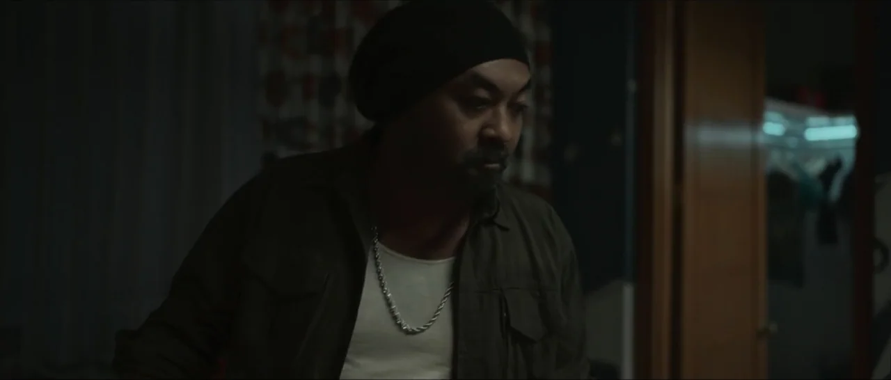 Innocent Vengeance (2023) movie still: medium — A dimly lit indoor hallway with a partially open door revealing a closet. A man in a beanie and…