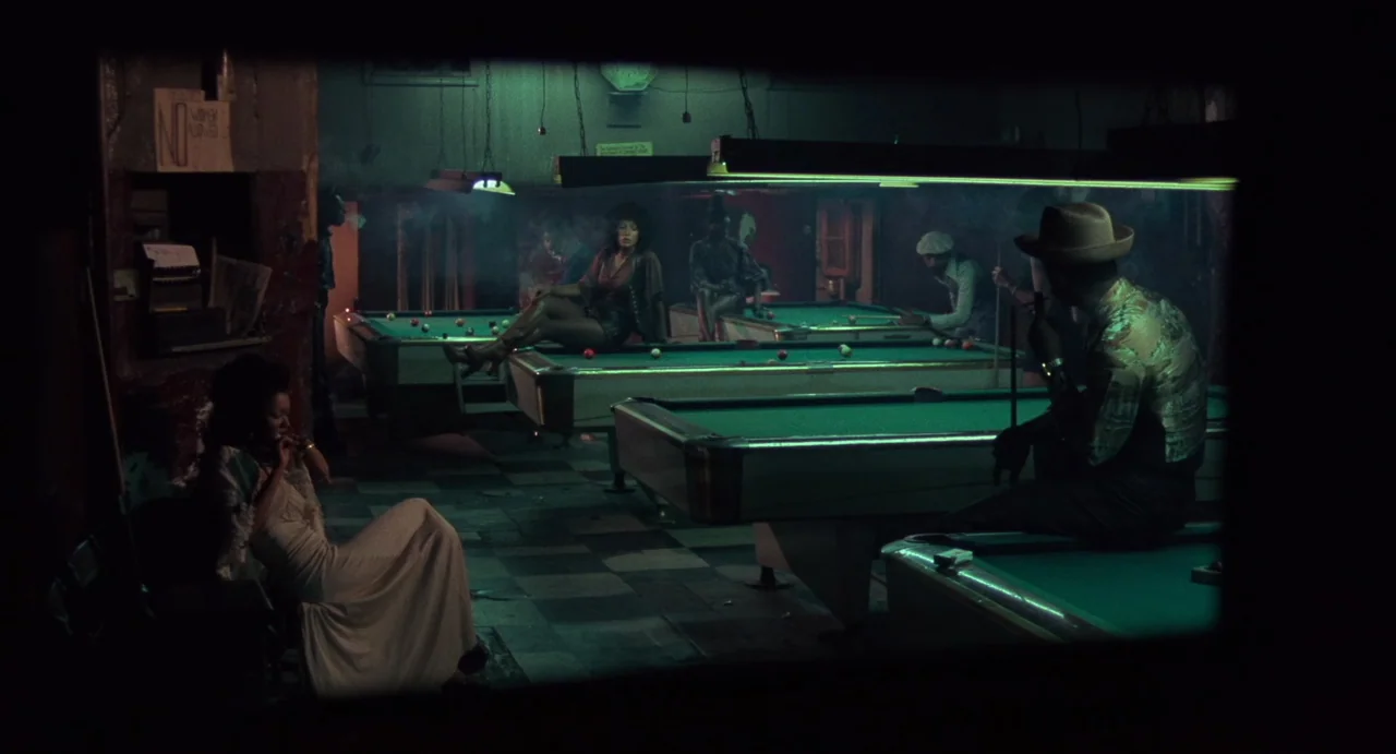 God Told Me To (1976) movie still: wide — A dimly lit 1970s billiard hall is filled with smoke and green-tinted fluorescent light. Several people…