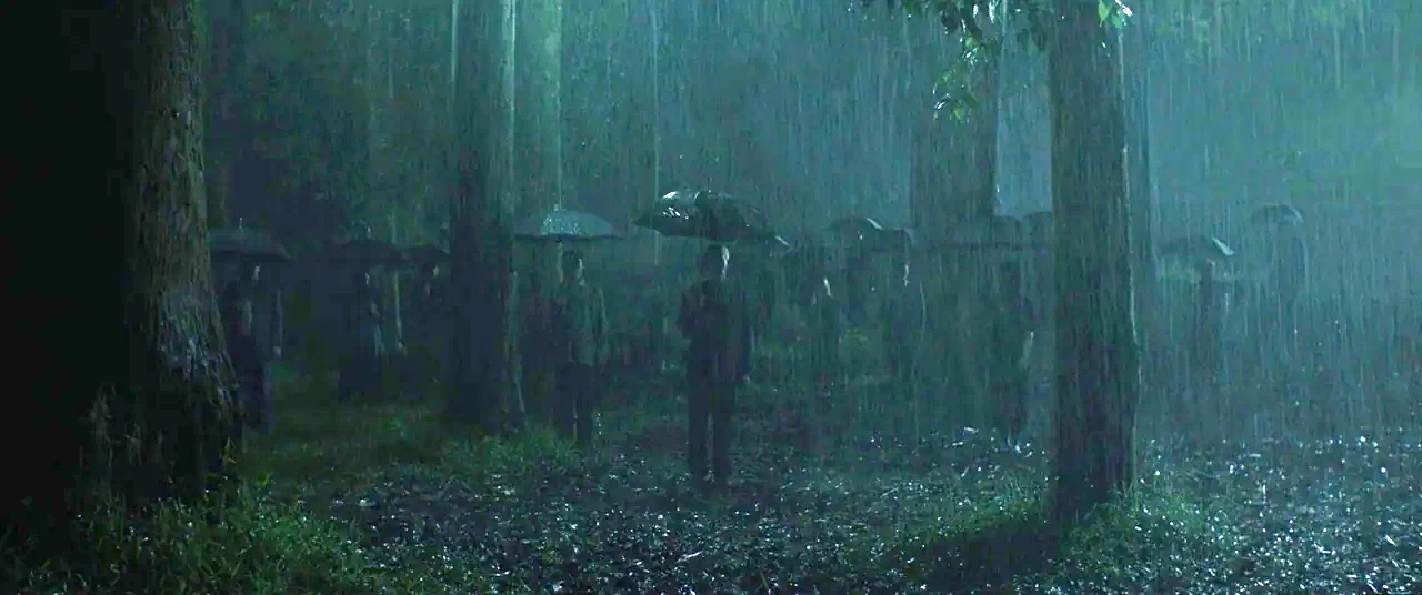 Satan’s Slaves (2017) movie still: wide — A dense group of people stands in a dark, rainy woods at night. They hold umbrellas while standing…