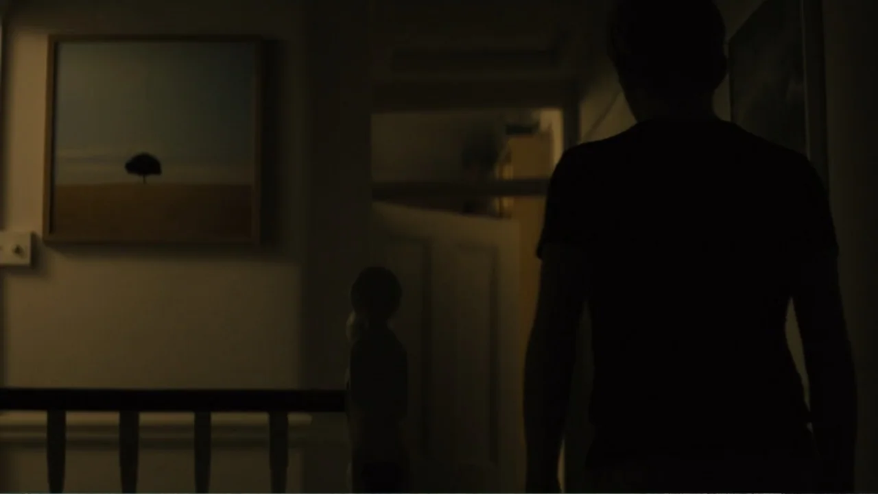 About Time (2013) movie still: medium — A dark, dimly lit staircase landing features a framed painting of a landscape. A person stands with their…