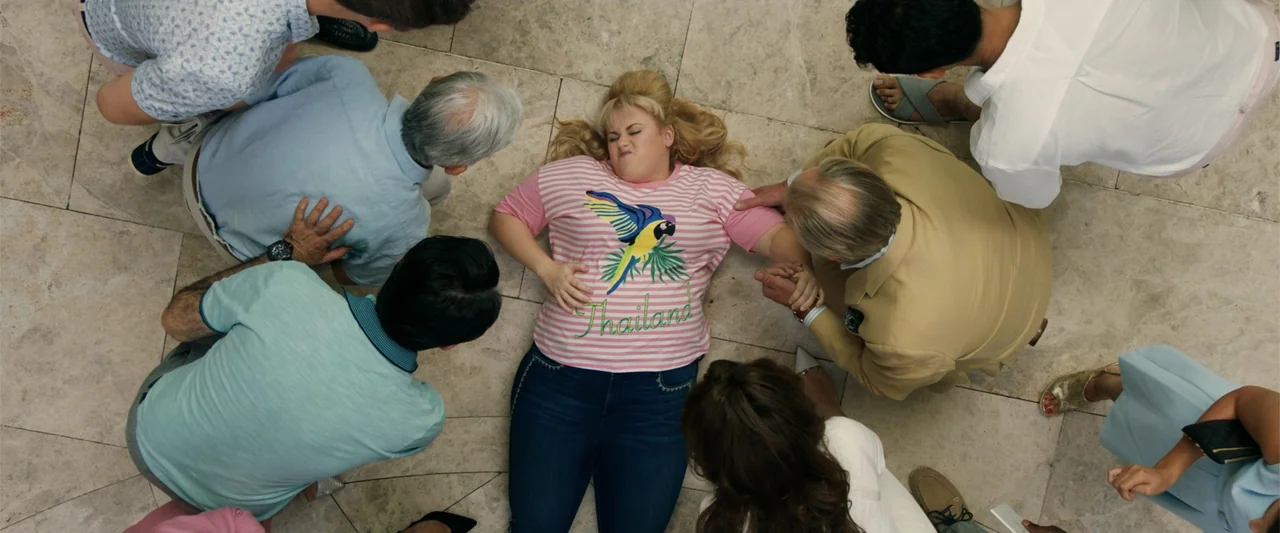 The Hustle (2019) movie still: fullbody — A polished marble floor serves as the setting for a gathering of several people. A blonde woman in a…