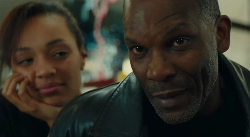 35 Shots of Rum (2008) movie still: medium — An interior space with a dimly lit background featuring blurred shapes and colors. A man in a leather…