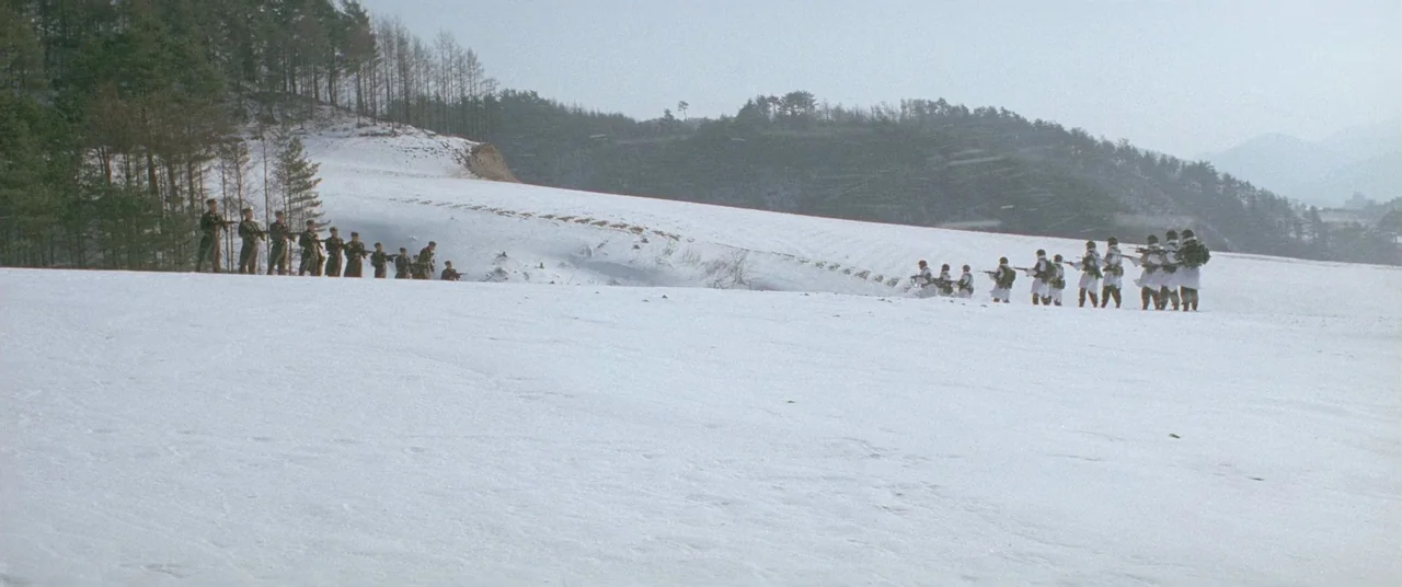 Joint Security Area (2000) movie still: wide — A wide view of a desolate, snow-covered landscape with rolling hills and distant trees. Two separate…