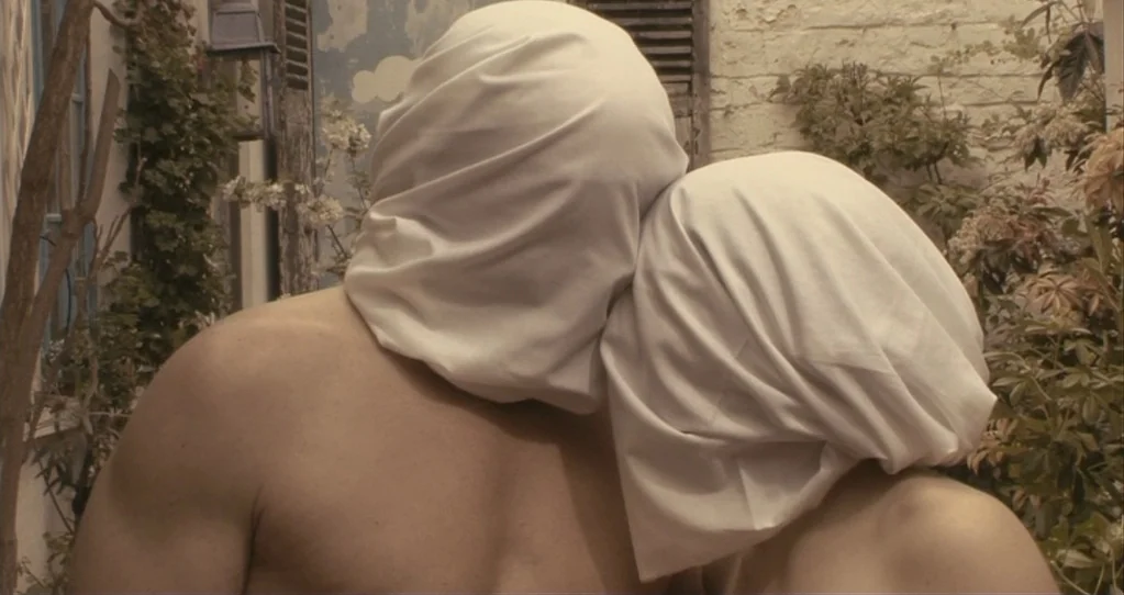 The Beaches of Agnès (2008) movie still: medium — An exterior stone wall with climbing vines forms the backdrop to the figures. Two people stand…