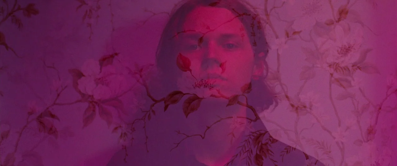 Woodshock (2017) movie still: closeup — A man is superimposed with a floral wallpaper pattern in a double exposure effect. He stands centrally…