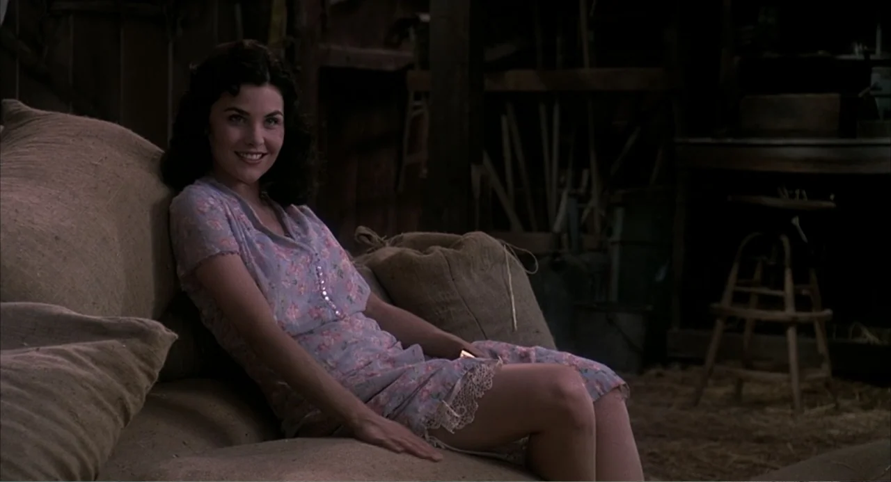 Of Mice and Men (1992) movie still: medium — A rustic barn interior features wooden walls and piles of large burlap grain sacks. A woman wearing a…