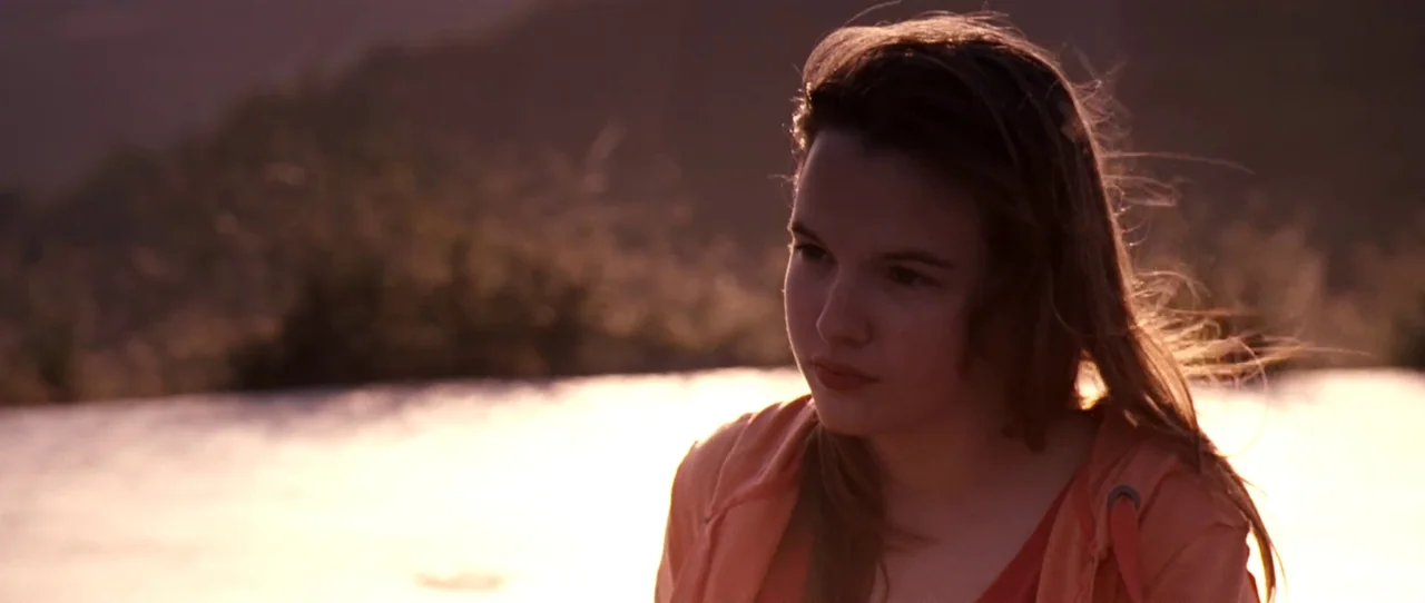 Little Birds (2011) movie still: closeup — A young woman stands outdoors against a backdrop of blurred hills during sunset. She faces slightly away…