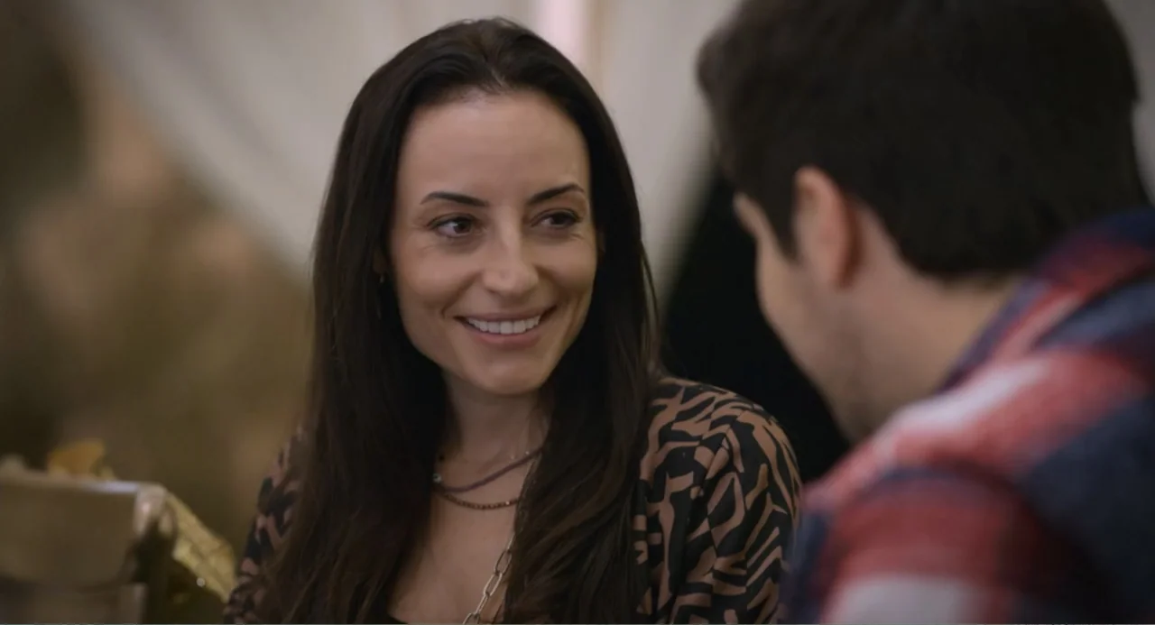 La posada (2023) movie still: medium — A well-lit indoor space featuring a woman smiling at her conversation partner. The woman sits across from a…