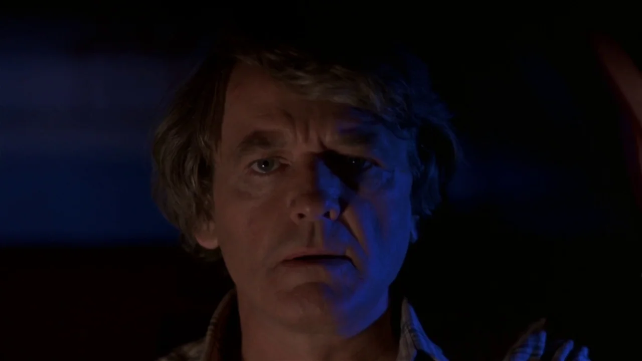 Creepshow (1982) movie still: closeup — The interior of a vehicle at night is shrouded in darkness. A man sits in the driver seat, illuminated by a…
