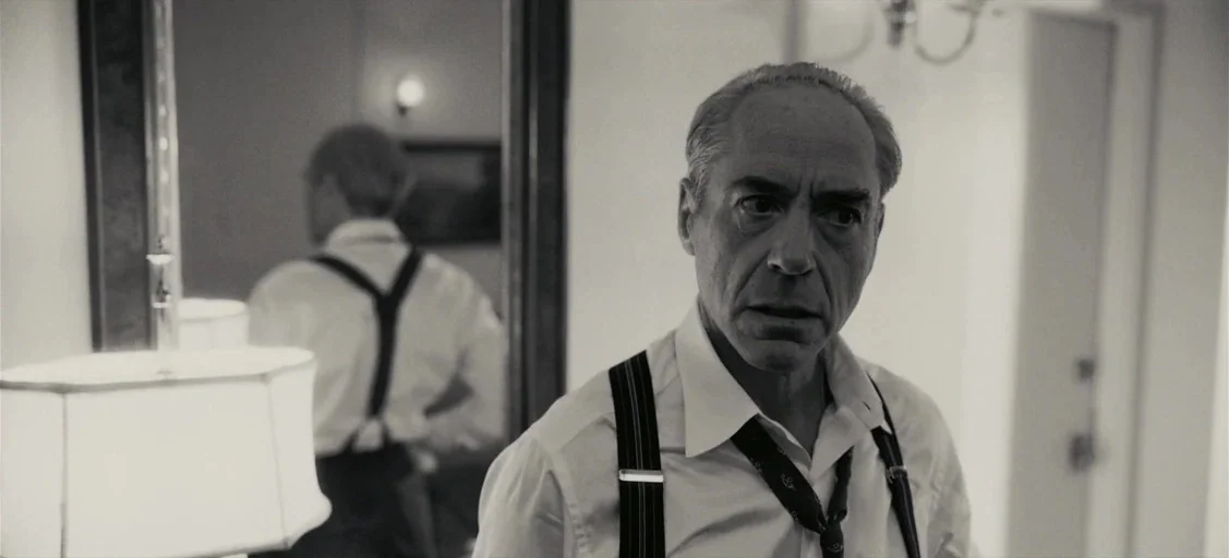Oppenheimer (2023) movie still: medium — A man in a dress shirt and suspenders looks into a wall mirror. His reflection is visible in the frame…