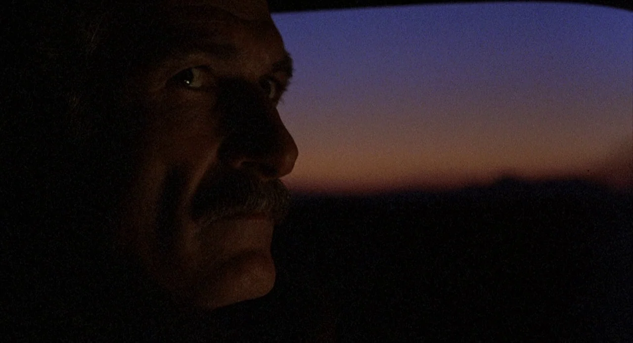 To Live and Die in L.A. (1985) movie still: closeup — The interior of a vehicle during dusk with a view of a sunset. An elderly man with a mustache…
