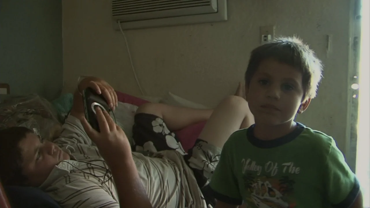 Homeless: The Motel Kids of Orange County (2010) movie still: medium — A bedroom contains a bed where two boys sit in relaxed postures. One boy…