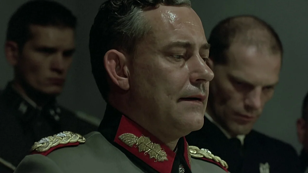 Downfall (2004) movie still: closeup — A dark, dimly lit concrete bunker interior provides a stark, oppressive backdrop. A man in a German officer…