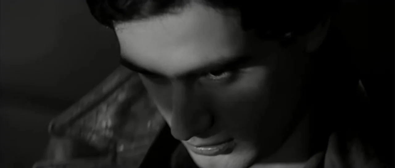13 Tzameti (2006) movie still: closeup — A dark indoor space where the subject's face is illuminated from the side. A young man with dark hair wears…