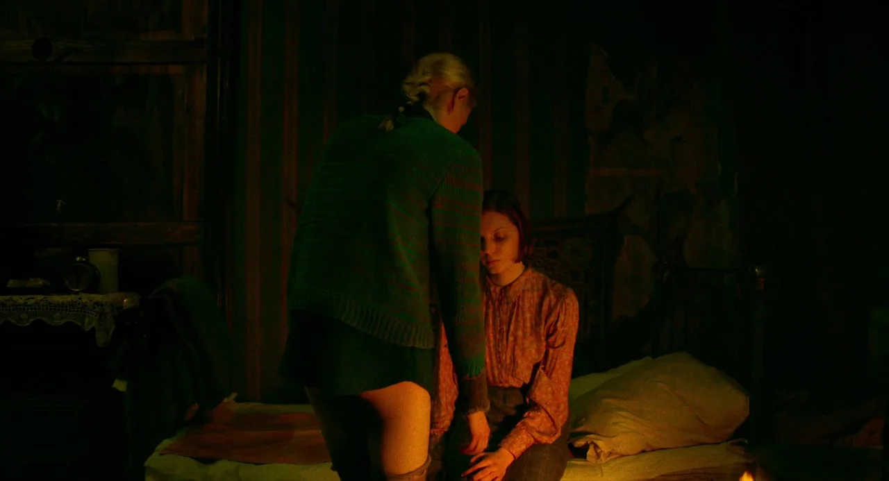 Beanpole (2019) movie still: medium — A dimly lit, cramped bedroom features dark patterned wallpaper and vintage furniture. A woman in a green…