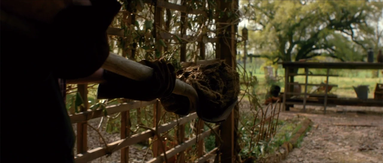 Jeepers Creepers 3 (2017) movie still: closeup — A garden area features a wooden trellis and a workbench in the background. A shovel loaded with…