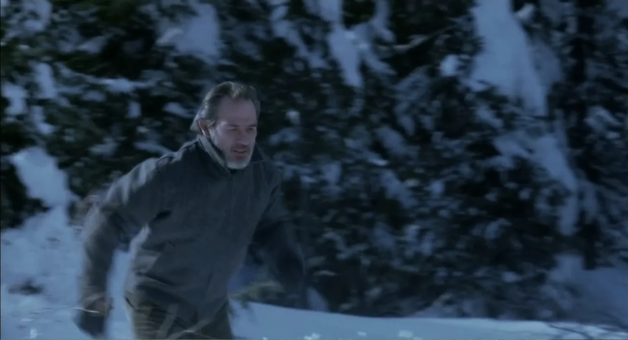 The Hunted (2003) movie still: medium — A dense, snow-covered forest provides the background for the outdoor setting. A middle-aged man in a dark…