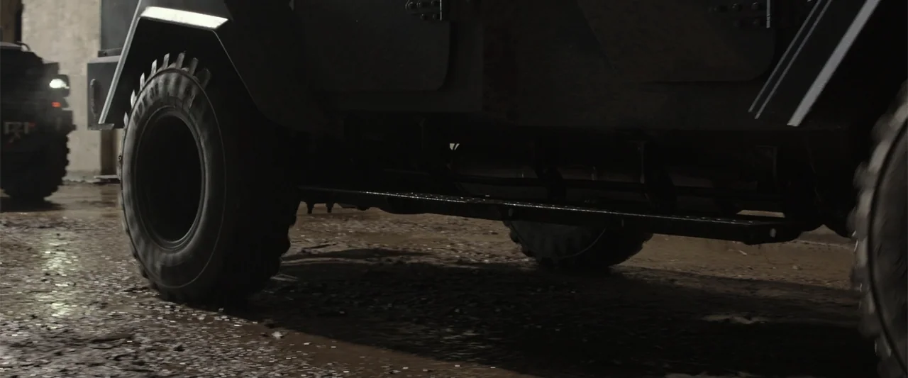 RoboCop (1987) movie still: medium — A dark industrial garage with a wet and dirty concrete floor. Two heavy armored vehicles roll slowly through…