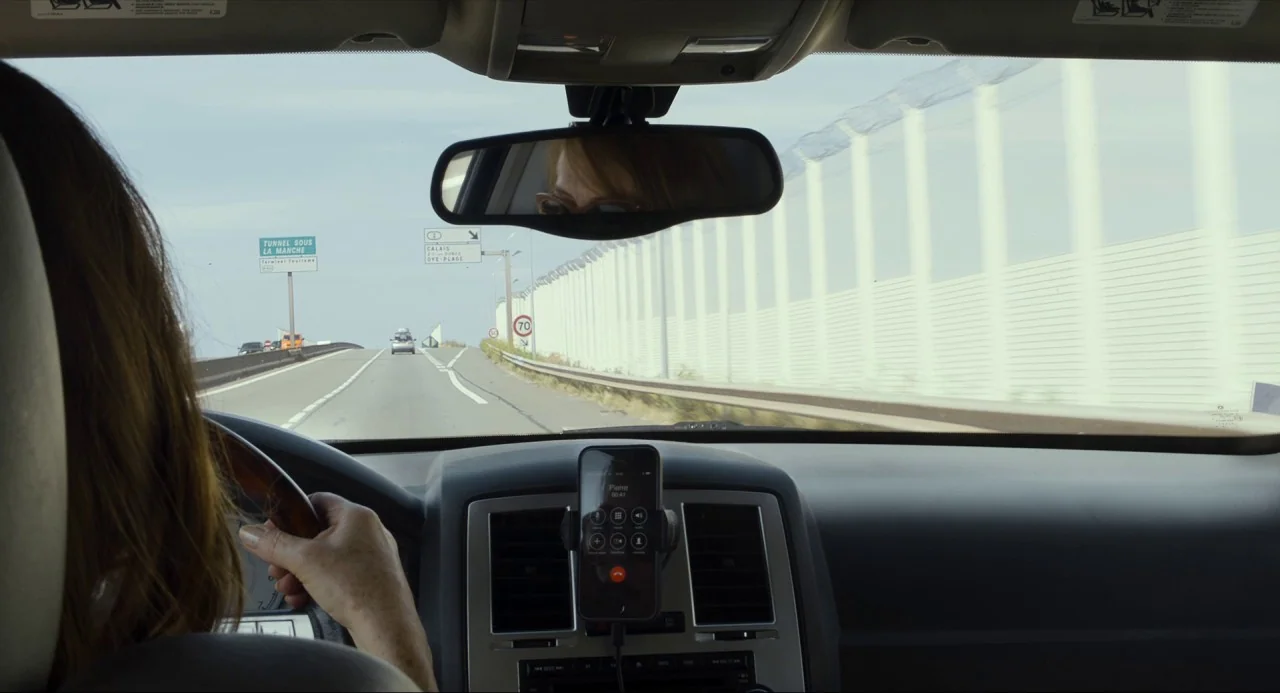 Happy End (2017) movie still: medium — The view from inside a moving car as it travels along a highway. A smartphone is mounted on the dashboard…