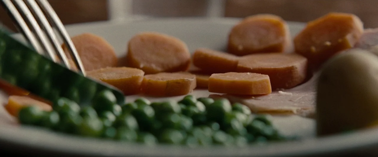 The Imitation Game (2014) movie still: closeup — A ceramic plate holds cooked carrots, green peas, and a portion of ham. A metal fork is inserted…