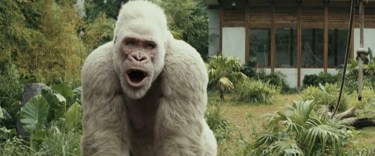 Rampage (2018) movie still: medium — An outdoor primate enclosure features lush tropical vegetation and a modern concrete structure behind. A large…
