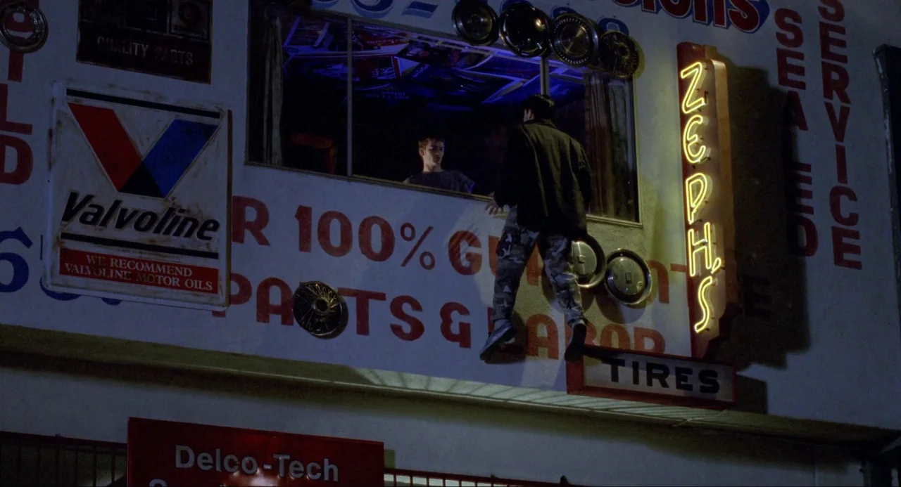 Buffy the Vampire Slayer (1992) movie still: medium — The exterior wall of a building is decorated with vintage metal signage and hubcaps. One man…
