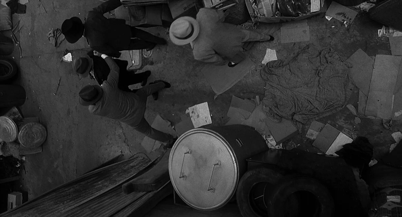 Dead Men Don’t Wear Plaid (1982) movie still: wide — A narrow outdoor passage littered with cardboard scraps, trash cans, and spare tires. Four men…