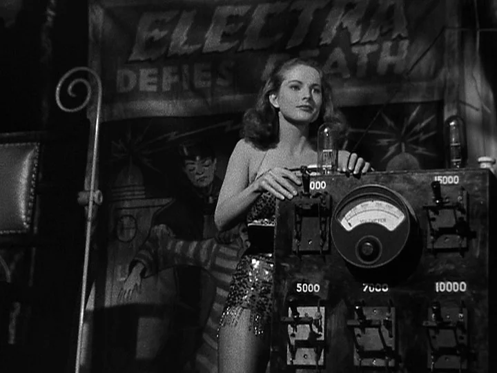 Nightmare Alley (1947) movie still: medium — A dark carnival booth displays a sign reading Electra Defies Death. A young woman stands behind an…