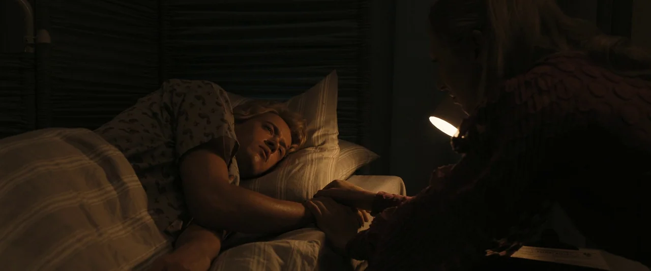 The Hunger Games: The Ballad of Songbirds & Snakes (2023) movie still: medium — A dimly lit room with gray striped bedding and a textured headboard.…
