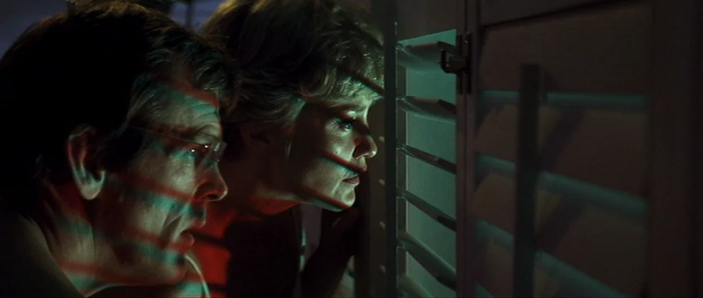 Cape Fear (1991) movie still: medium — A dark room contains two people looking outside through white painted window shutters. Horizontal bands of…