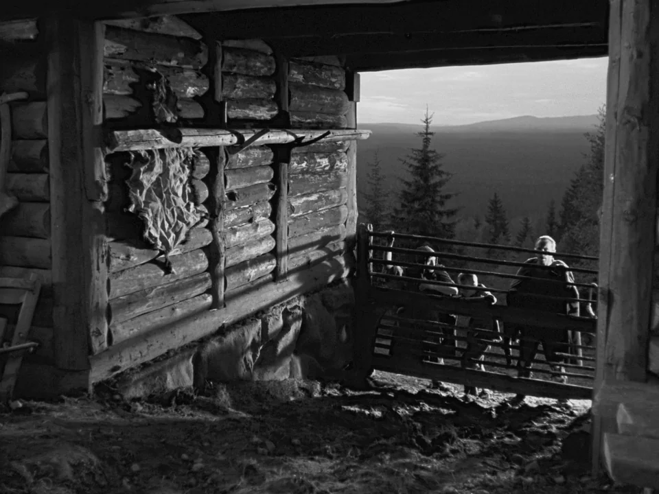The Virgin Spring (1960) movie still: wide — A rustic log barn features a dried animal hide pinned against the inner wall. Three people stand at a…