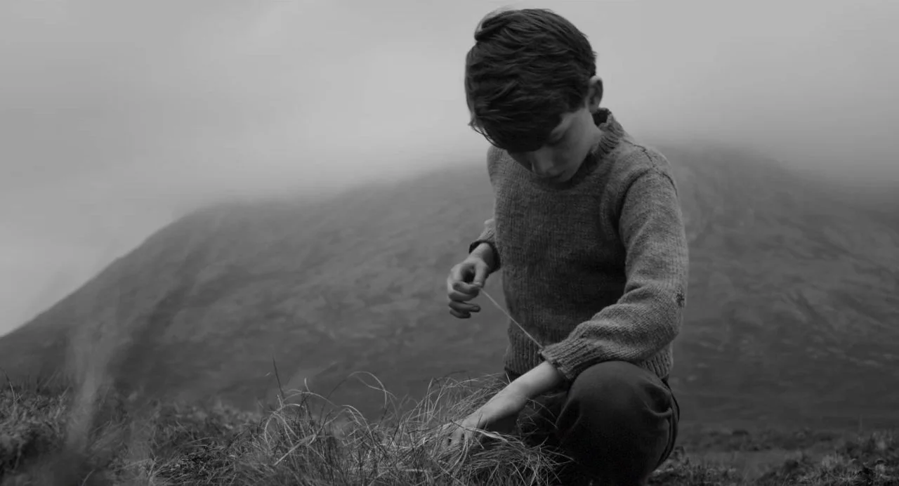 Song of Granite (2017) movie still: medium — A boy kneels in a grassy field on a mist-covered mountain hillside. He holds a thin string between his…