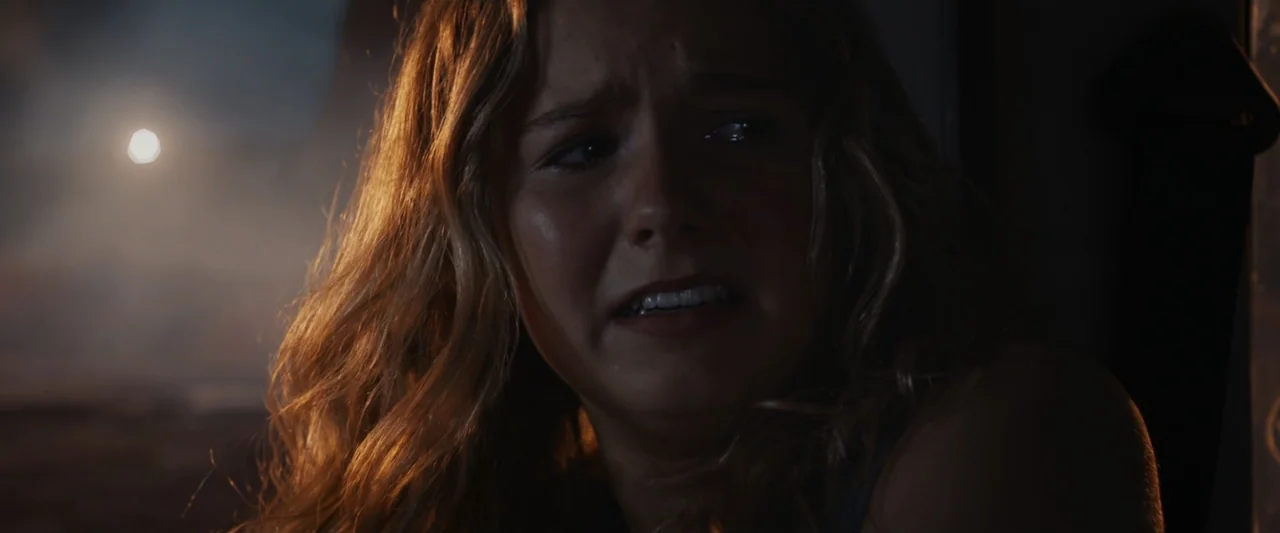 Mia and the White Lion (2018) movie still: closeup — A dark outdoor space is lit by a warm, flickering light source. A young woman with wavy hair…