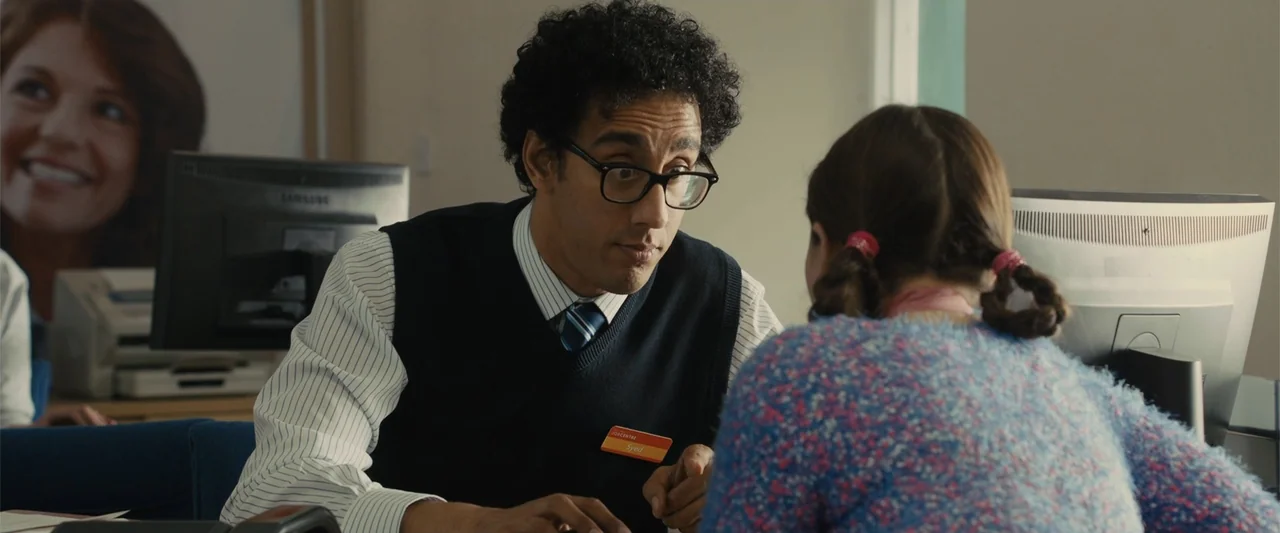Me Before You (2016) movie still: medium — A sterile professional office features a computer monitor and a nametagged employee. A man sits across…
