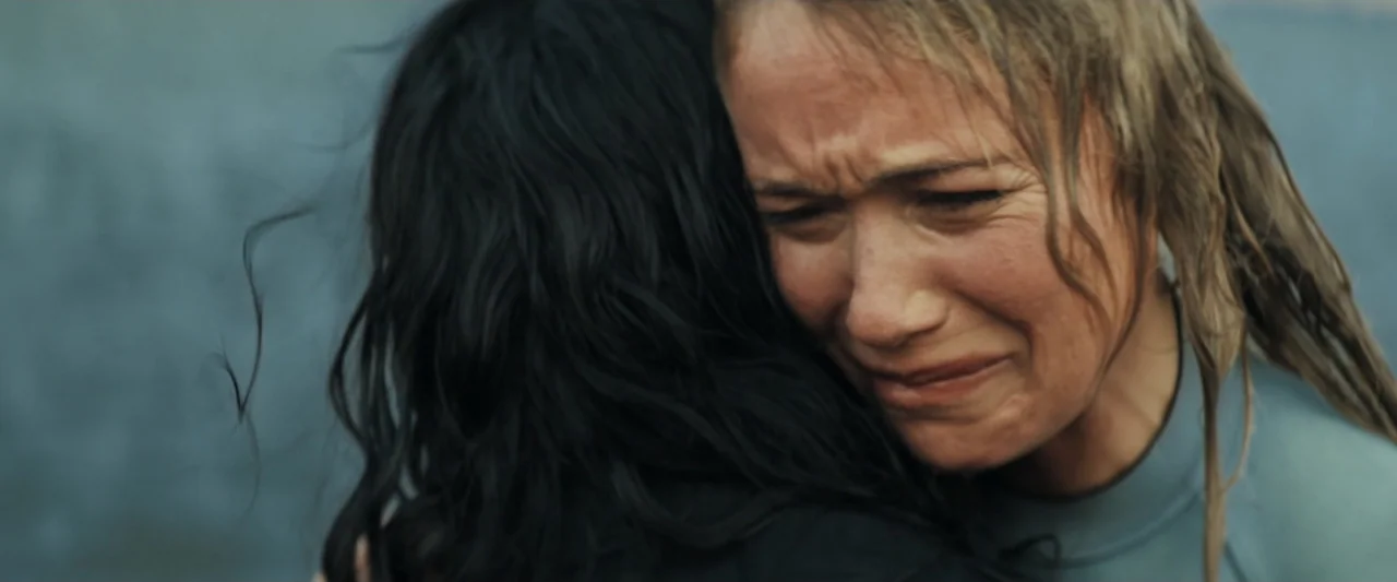 Great White (1998) movie still: closeup — Two women stand on a beach under an overcast sky. One woman with blonde hair holds the other woman tightly…