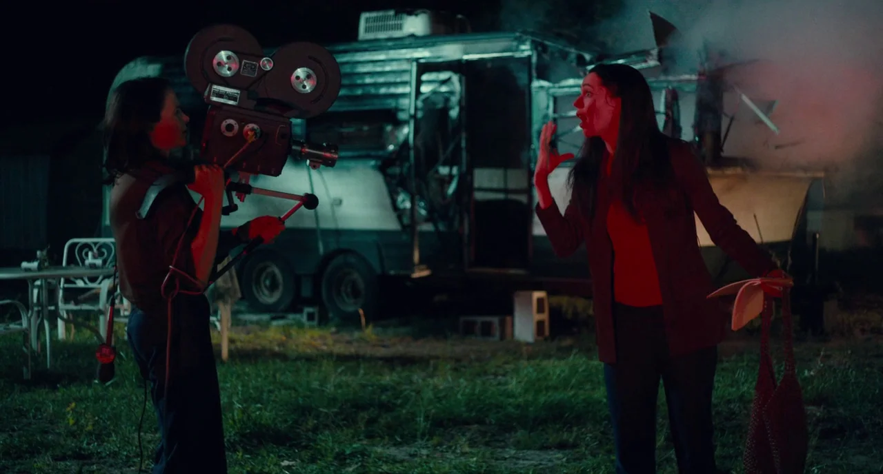 Christine (2016) movie still: medium — A nighttime scene in a trailer park with a smoking damaged vehicle in background. A woman operates a…