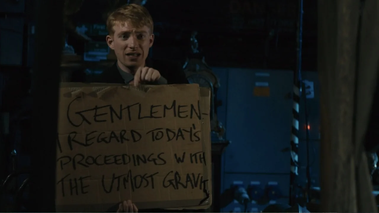 About Time (2013) movie still: medium — A dimly lit indoor space with indistinct machinery and equipment in the background. A young man holds a…