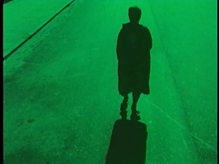 The Cage (1964) movie still: fullbody — A person walks alone along a dark asphalt road surface. The entire scene is bathed in a saturated green…