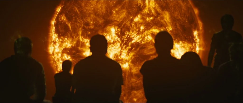 Sunshine movie still: wide — Several silhouetted figures stand before a gargantuan, burning star visible through a large portal. The group stares at…