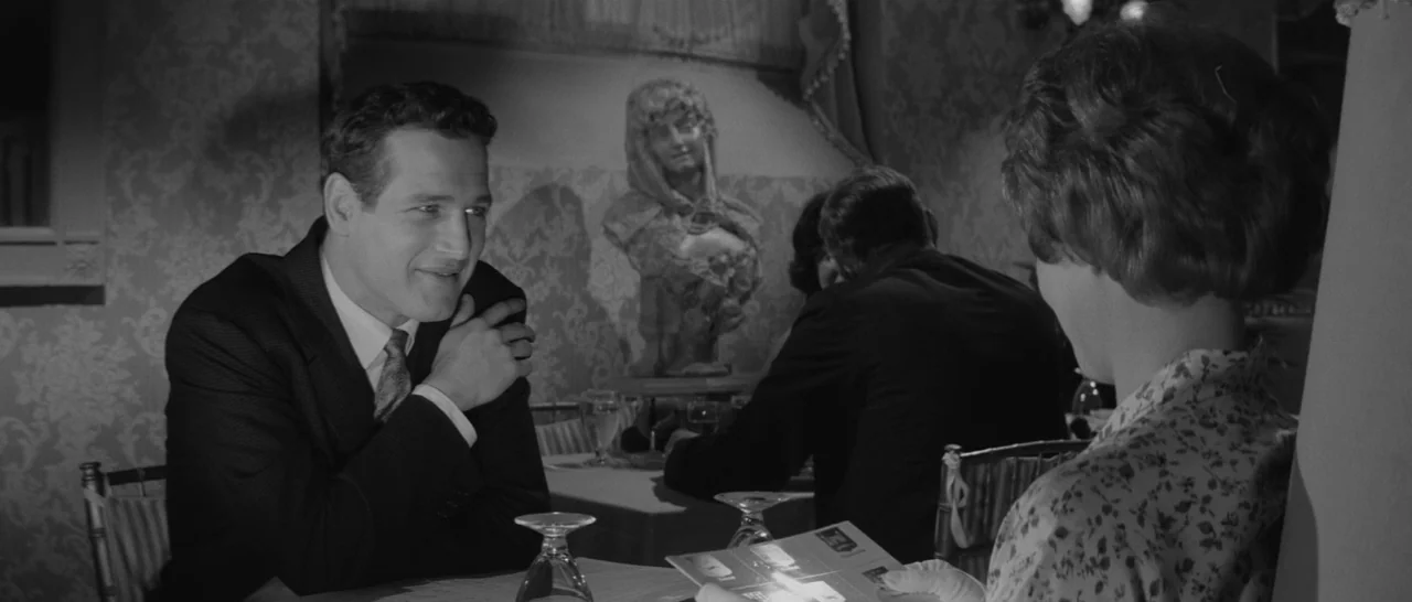 The Hustler (1961) movie still: medium — A dimly lit room features patterned wallpaper and an ornate decorative bust. A man in a suit sits across…