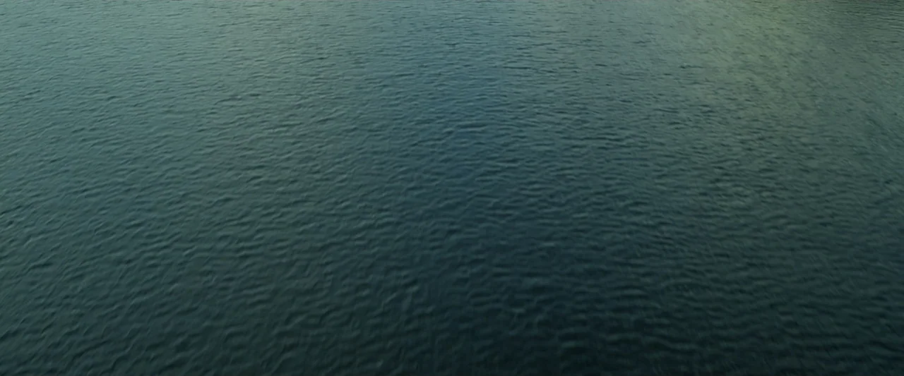 Great White (1998) movie still: establishing — A vast expanse of dark, rippling water fills the frame completely. The surface displays rhythmic wave…