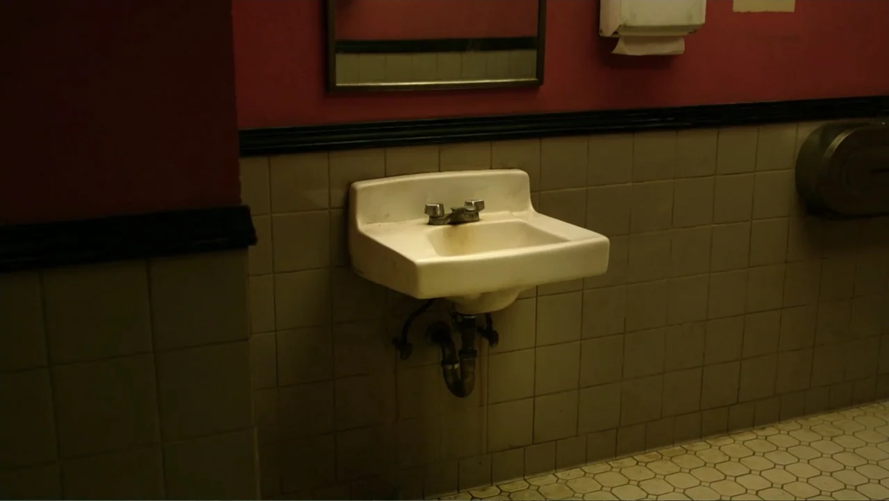 Ghostbusters (2016) movie still: medium — A public restroom features tan tiled walls and a deep red painted upper section. A wall-mounted porcelain…