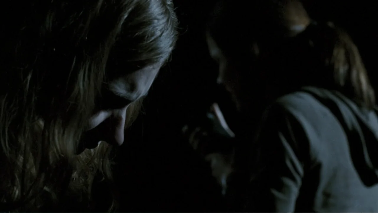 28 Weeks Later (2007) movie still: closeup — A dark indoor space where the background is completely blacked out. Two young women face each other in…