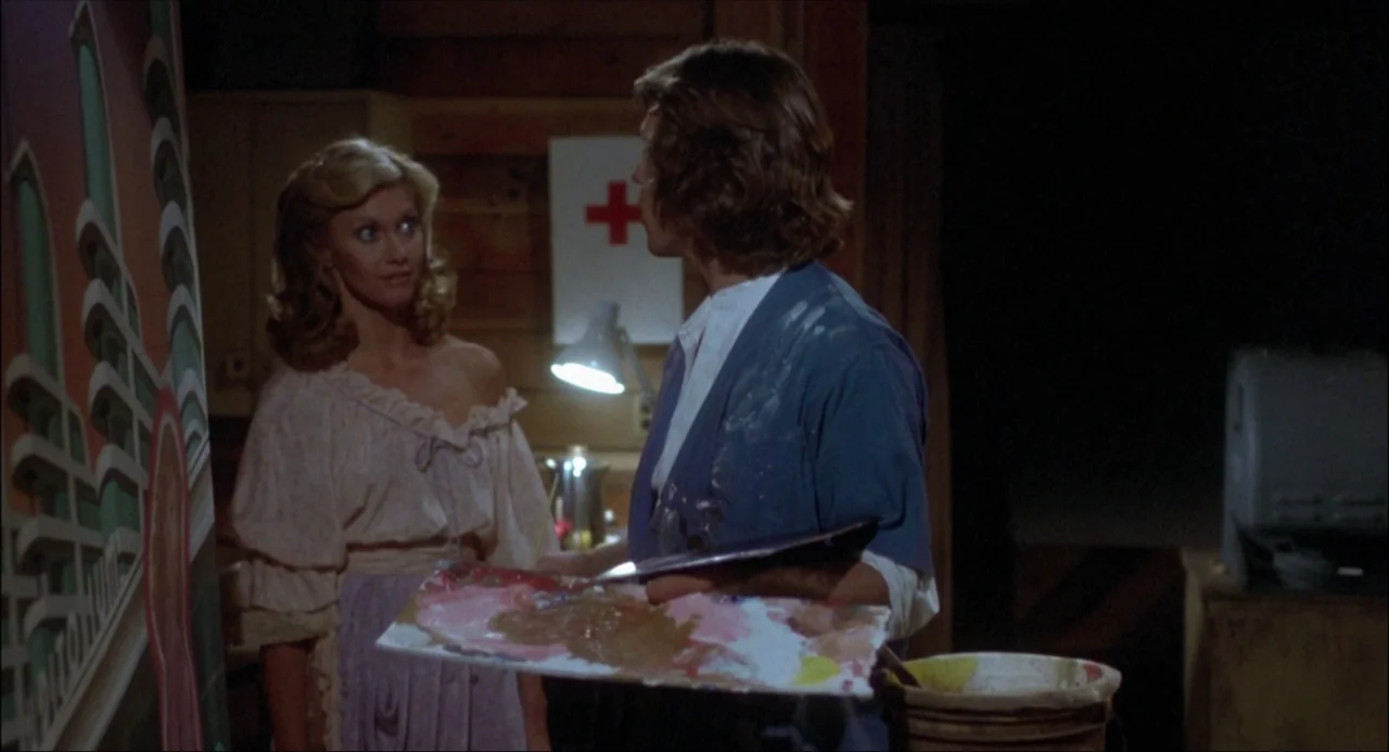 Xanadu (1980) movie still: medium — An interior space contains a large upright painting and a desk lamp on a wall. A man in a stained shirt holds a…