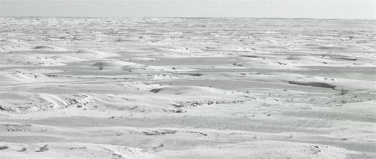 The Last Battle (1983) movie still: establishing — A vast, flat expanse of sand dunes stretches to the distant horizon line. Sparse desert…