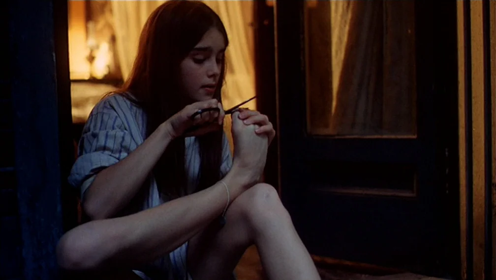 Pretty Baby (1978) movie still: medium — A dark, wood-framed doorway opens into a dimly lit room with soft curtains hanging. A young girl sits on…