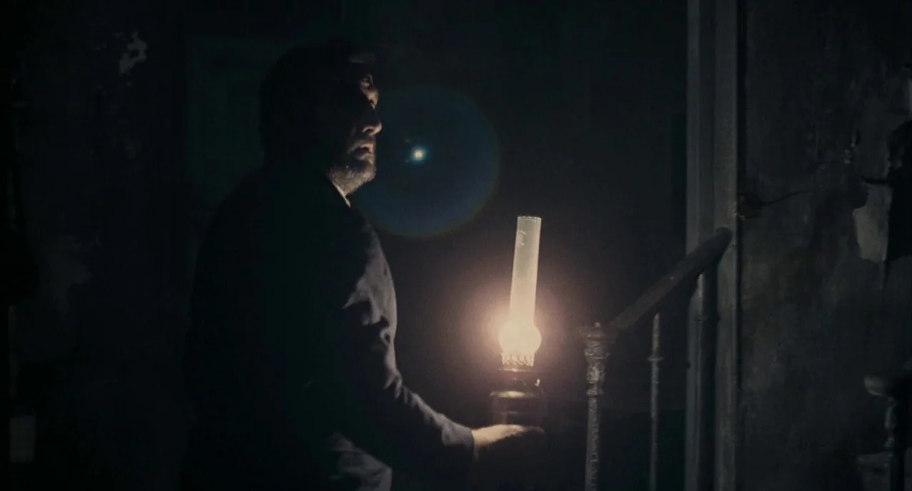 The Army of Shadows (1969) movie still: medium — A dark, shadowed indoor stairwell features peeling paint and weathered wooden architecture. A man…